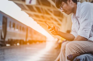 Cep telefonu ve çantalı bir adam tren bekliyor. İş ve seyahat konsepti..