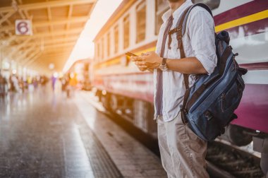 Cep telefonu ve çantası olan bir adam tren bekliyor. İş ve seyahat konsepti..