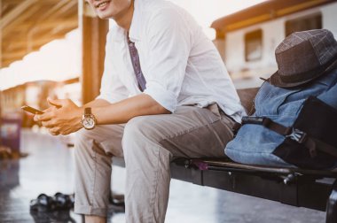 Cep telefonu ve çantalı bir adam tren bekliyor. İş ve seyahat konsepti..