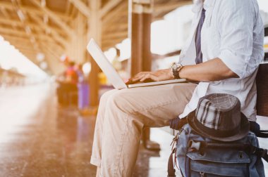 Dizüstü bilgisayarlı ve çantalı bir adam tren bekliyor. İş ve seyahat konsepti..