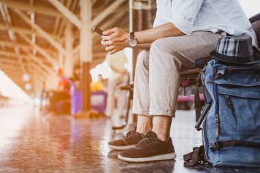 Cep telefonu ve çantalı bir adam tren bekliyor. İş ve seyahat konsepti..