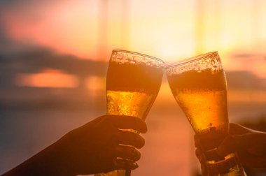 Yazın gün batımında barda bira şişesi ve çıngırak tutan iki el.