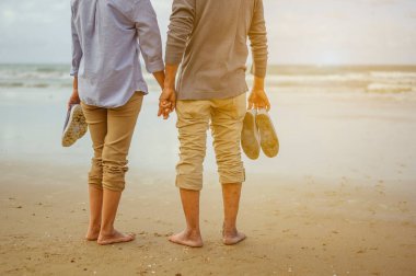 Gün batımında sahilde el ele tutuşan yaşlı çift emeklilik konseptinde hayat sigortası yapmayı planlıyor..