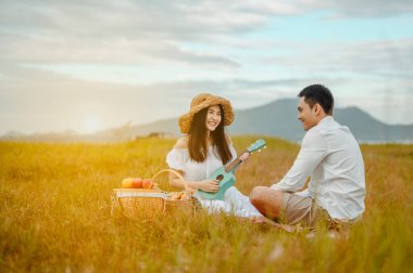 Mutlu aşıklar çayırda oturup birbirlerine şefkatle bakıyorlar kadınlar piknik kutularını dinleyen erkeklerle gitar çalıyorlar. Birbirlerine sevgiyle ve gülümsemeyle bakıyorlar..