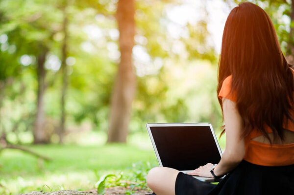  Женщина сидит в парке на зеленой траве с ноутбуком, ноутбуком, руками на клавиатуре. Компьютерный макет. Ученик учится на улице. Копирование текста
