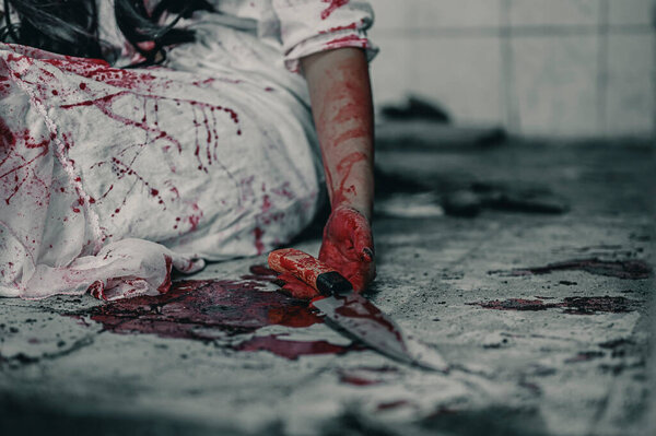 Девушка-зомби в крови сидит с ножом в руке, испачканным кровью, с пытками обиды, и просит помощи в заброшенном здании. Концепция убийства на Хэллоуин.