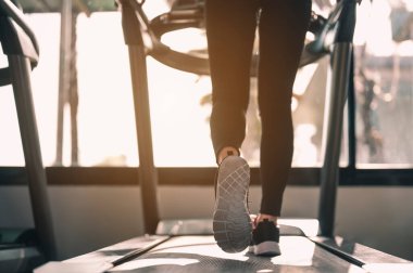Spor, spor, spor, yaşam tarzı ve sağlıklı konsept. Gün batımında sağlık ve güç için spor salonundaki koşu bandında yürüyen kadınların bacakları ve ayakları yakın plan..