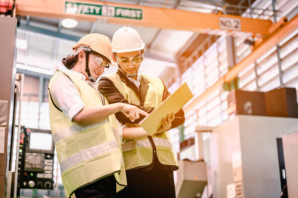 Male and female industrial engineers wearing helmets are using laptops to study and talk about new projects in industrial plants. They acted happily and professionally. Engineering and architecture technology for factory industry concept.