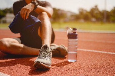 Fitness, koşu, egzersiz, yaşam tarzı ve sağlıklı konsept. Genç adam futbol sahasının etrafındaki koşu pistinde koşuya hazırlanmak için vücudunun her yerini giydi ve su içti..