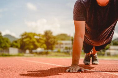Fitness, koşu, egzersiz, yaşam tarzı ve sağlıklı konsept. Genç adam futbol sahasının etrafındaki koşu pistinde koşuya hazırlanmak için vücudunun her yerini giydi..