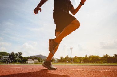 Fitness, koşu, egzersiz, yaşam tarzı ve sağlıklı konsept. Genç adam futbol sahasının etrafındaki koşu pistinde koşuya hazırlanmak için vücudunun her yerini giydi..