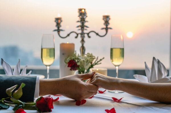 Couple holding hands having a dinner date at restaurant in sunset view. Valentine's, Couple, Honeymoon, Dinner, Wine, Romantic concept. 