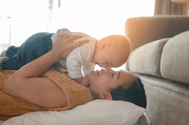 Anne sakin bir şekilde yatar ve çocuklarını evdeki oturma odasında öğle yemeğine yatırır. Aile, ebeveyn, oğul, bebek, mutlu, yaşam tarzı konsepti.