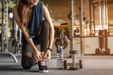 Kadınlar ellerini ayakkabılarını bağlamak için kullanıyor, halterleri ve bir şişe suları var. Gün batımında spor salonunda egzersiz yapmaya hazırlan. Spor, spor, spor, yaşam tarzı ve sağlıklı konsept.