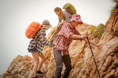 Dağcı erkek ve kadın yürüyüşçülerden oluşan bir ekip dağcılık başarısı için kırmızı bayraklarla tepeye tırmanırken birbirlerine yardım etmek için el ele tutuşuyorlar. Yürüyüş, yürüyüş, takım, dağ, tırmanış, aktivite konsepti.