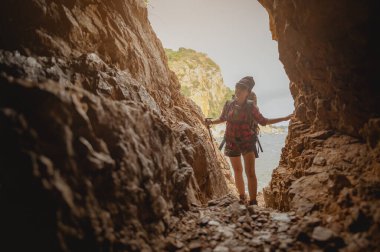 Gün batımında mağarada uçuruma tırmanan kadın yürüyüşçünün yan görüntüsü. Kadın, yürüyüş, yürüyüş, dağ, mağara, aktivite konsepti.