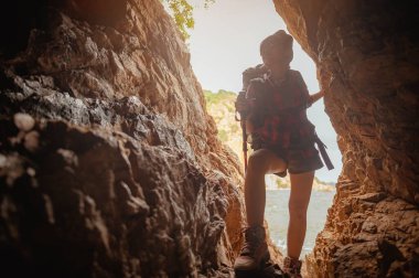 Gün batımında mağarada uçuruma tırmanan kadın yürüyüşçünün yan görüntüsü. Kadın, yürüyüş, yürüyüş, dağ, mağara, aktivite konsepti.