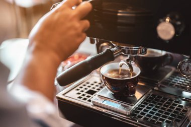 Yakın plan kahve makinesi, kahve barmeninin akşam güneşinde koyu beyaz bardakla kahve çıkarmasını sağlıyor. kahve, çıkartma, derin, makine, yapım, barista konsepti. 