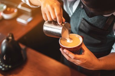 Kahve barmeninin kahve fincanına buğulanmış süt doldurup güzel latte sanatları yaptığı yakın plan çekimler. kahve, çıkartma, derin, fincan, sanat, barista konsepti. 