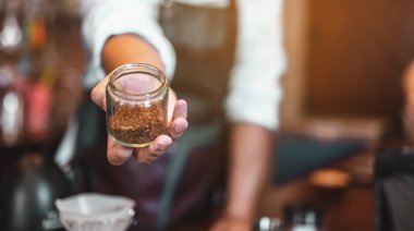 Kahveci adamın elinde öğütülmüş bir kahve çekirdeği var. Erkek elleri masaya bir fincan kahve koyuyor. Kahve, barista, çıkarma, servis, kafe, yaşam tarzı konsepti..