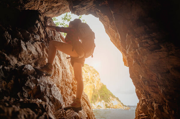 Side view of woman hiker climbing on the cliff at cave in sunset. Woman, hiking, hikers, mountain, cave, activity concept.