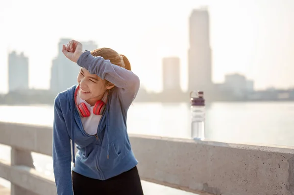 Young woman wipes sweat after a morning workout in the city. A city that lives healthy in the capital Rear view of the city Exercise, fitness, jogging, running, lifestyle, healthy concept.