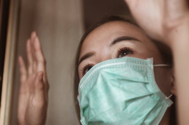 Pencerede maske takan kadın salgın durumunun yakında düzelmesini bekliyor. Coronavirus, covid-19, Home (WFH), Social Mesafe, Karantina, Enfeksiyon Önleme Konsepti.