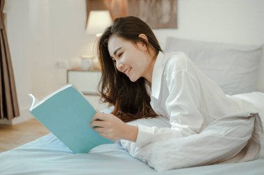 Asya 'nın evinde yaşayan, tatilde yatak odasında kitap okuyan genç bir kadın. Asya, Asya, rahatla, yalnız, teknoloji, yaşam tarzı konsepti.