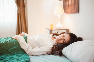 Genç bayan Asya sabah dinlenmiş olarak uyanır ve tatilde yatak odasında dinlenir. Asya, Asya, rahatla, yalnız, teknoloji, yaşam tarzı konsepti.