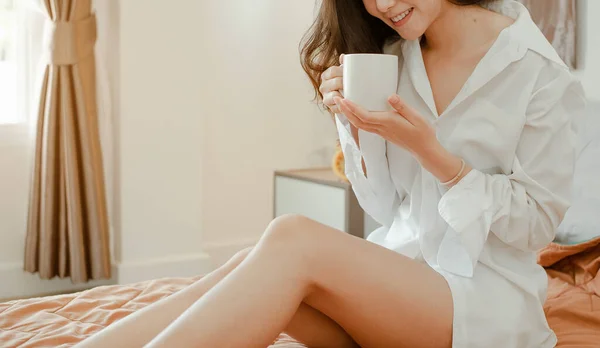 Young woman asia living at home relaxing and drinking cup of hot coffee in the bedroom on holiday. Asian, asia, relax, alone, technology, lifestyle concept.