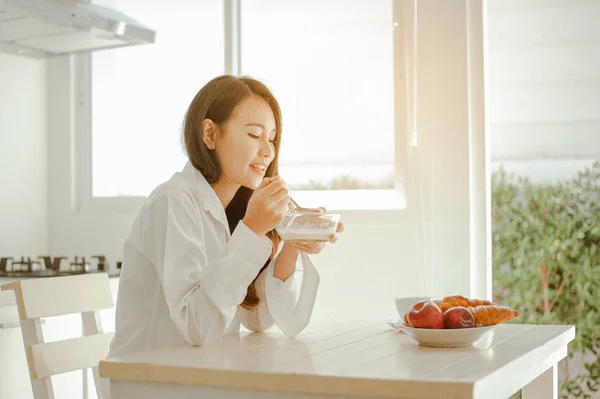 Young woman asia wake up refreshed in the morning and relaxing eat coffee, cornflakes, bread and apple for breakfast at house on holiday. Asian, asia, relax, breakfast, refresh, lifestyle concept.