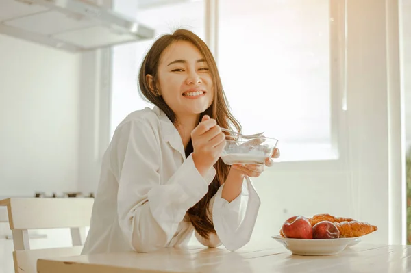Genç bayan Asya sabah dinlenmiş olarak uyanır ve dinlenir kahve, mısır gevreği, ekmek ve elmayı tatilde evde kahvaltı için yer. Asya, Asya, rahatla, kahvaltı, ferahlatıcı, yaşam tarzı konsepti.