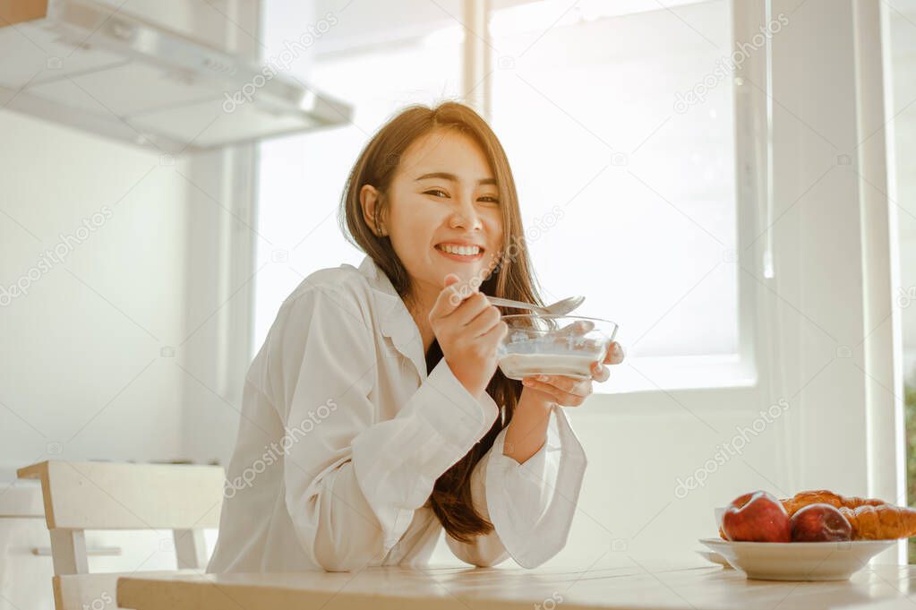 Young woman asia wake up refreshed in the morning and relaxing eat coffee, cornflakes, bread and apple for breakfast at house on holiday. Asian, asia, relax, breakfast, refresh, lifestyle concept.