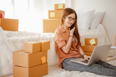 Genç Asyalı kadın müşterilerle çevrimiçi ürün satmak ve müşterilere teslimat yapmak için konuşuyor. İş sahibi, KOBİ, taşımacılık, evden (WFH), serbest, başlangıç konsepti.