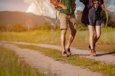 Geniş bir tarlada yaşayan Asyalı genç bir çift ormanı keşfetmek için sonbahar mevsiminde orman yolunda bir tatil aktivitesi olarak yürüyor. Yürüyüş, yürüyüş, takım, orman, kamp, aktivite konsepti.