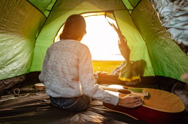 Çadırın içinde yeni uyanan Asyalı kadın sonbahar mevsiminde ormanda tatil amaçlı sabah güneşinin doğuşunu izliyordu. Yürüyüş, yürüyüş, yalnız, orman, kamp, aktivite konsepti.