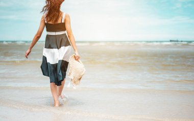 Ellerinde şapkası olan mutlu Asyalı kadınlar yalınayak yürüyorlar. Rüzgarın esmesini bekliyorlar ve plaj tatilinin tadını çıkarıyorlar. Plaj, yaz, kaldırma stili, pozitif ruh hali, seyahat, rahatlama konsepti.