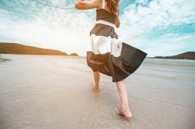 Ellerinde şapkası olan mutlu Asyalı kadınlar yalınayak yürüyorlar. Rüzgarın esmesini bekliyorlar ve plaj tatilinin tadını çıkarıyorlar. Plaj, yaz, kaldırma stili, pozitif ruh hali, seyahat, rahatlama konsepti.