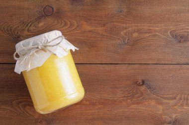 Cam kavanozdaki sarı bal kırsal bir şekilde paketlenmiştir. Kahverengi ahşap bir arka planda