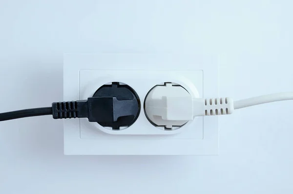 Electrical plugs from electrical appliances white and black are included in the socket on a white background. Close-up.