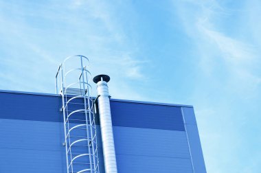 Endüstriyel mavi bir binanın ön cephesinde metal bir merdiven ve havalandırma borusu. Aşağıdan görüntüle.