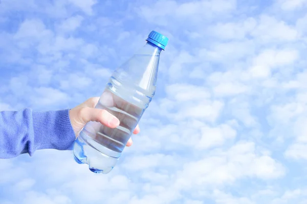 白人女性の手にプラスチック製の水ボトル 雲のある青空を背景に — ストック写真