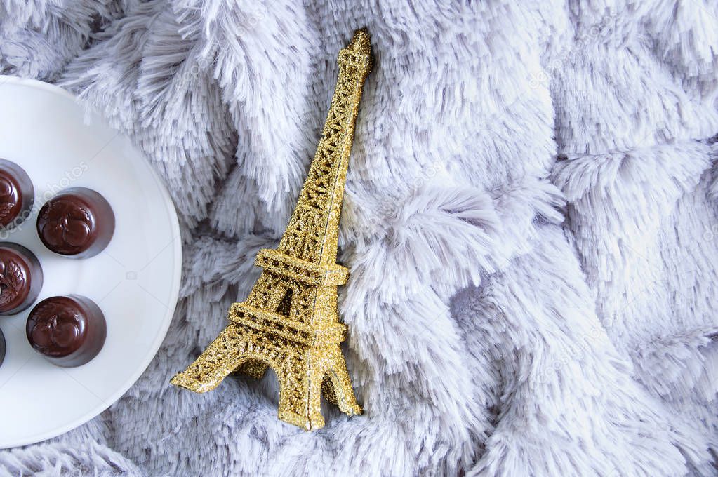 Chocolates on a white plate and a statuette of the Eiffel Tower on a fur plaid.