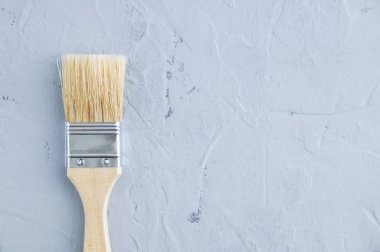 Gri beton arka planda ahşap bir sapla yeni fırça boyuyor..