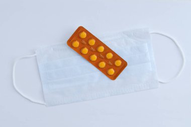 Koruyucu yüz maskesi ve beyaz arka planda sarı su toplayan haplar. Yukarıdan görüntüle.