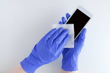 Cerrahi eldivenli beyaz bir kız dezenfektan mendille beyaz bir akıllı telefonu siliyor..