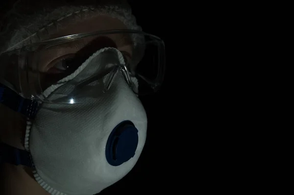 Female doctor in a protective mask and glasses at night on a black background.