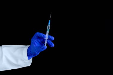 Koruyucu mavi eldivenli bir el siyah arka planda iğnesi olan bir şırınga tutar..