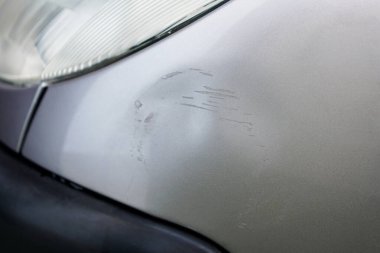 Gümüş gri arabanın üzerinde çiziklerle dolu bir kazaydı. Kaza, otopark ya da trafik yüzünden hasar görmüş bir araba..