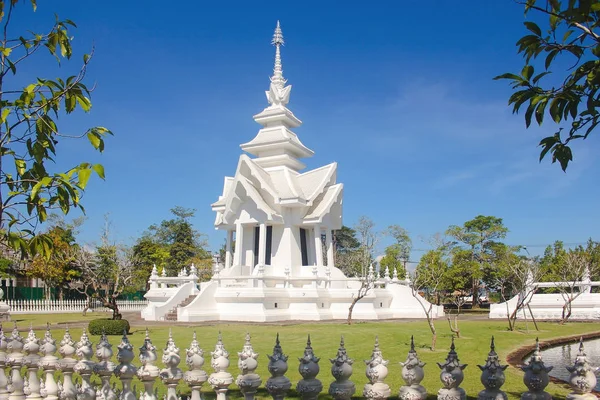 Buddhistisk byggnad med skiktat tak i Wat Rong Khun eller Vita templet omgivet av träd och balster med blå himmel — Stockfoto